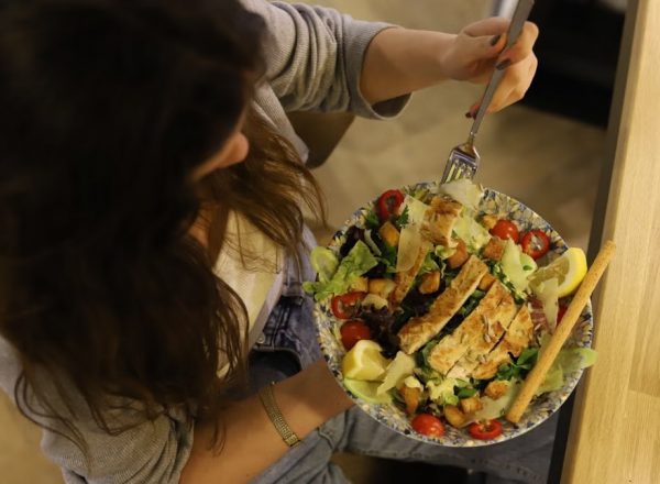 Overhead view of a woman eating a chicken salad balancing health with deliciousness.