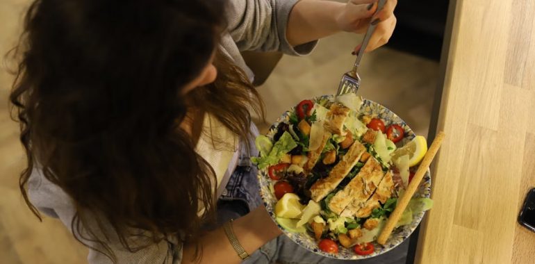 Overhead view of a woman eating a chicken salad balancing health with deliciousness.