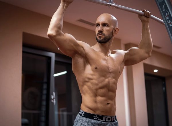 A bald, muscular man performing exercise on gym equipment indoors.